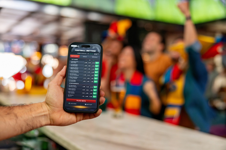 Image of man's hand holding mobile phone with betting app open